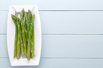 Fresh cooked green asparagus served on plate, photographed overhead on light blue wood with copy space on the side