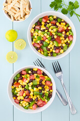 Mexican style colorful fresh vegetable salad made of beans, corn, tomato and bell pepper served in bowls, photographed overhead on light blue wood (Selective Focus, Focus on the salad)