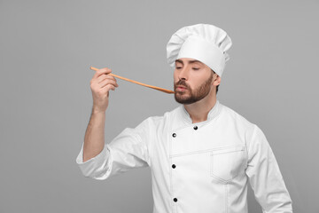Mature chef with spoon tasting dish on grey background, space for text