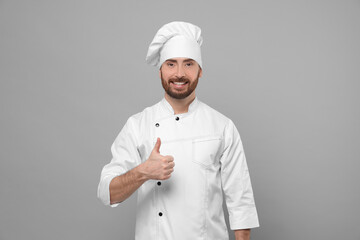 Smiling mature male chef showing thumbs up on grey background