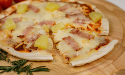 Closeup top view studio shot of round hot oven baked tasty delicious Italian homemade ham pineapple original Hawaiian soft bread crust pizza on wooden plate pan with tomatoes and ketchup on table
