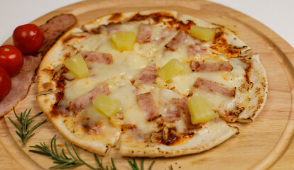 Closeup top view studio shot of round hot oven baked tasty delicious Italian homemade ham pineapple original Hawaiian soft bread crust pizza on wooden plate pan with tomatoes and ketchup on table