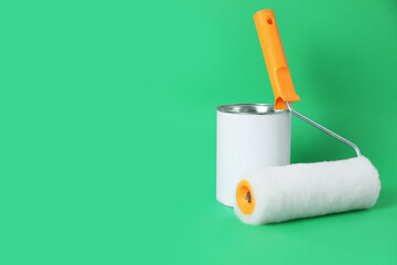 Can of orange paint and roller brush on green background. Space for text