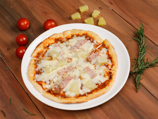 Closeup top view studio shot of round hot oven baked tasty delicious Italian homemade ham pineapple original Hawaiian soft bread crust pizza on wooden plate pan with tomatoes and ketchup on table
