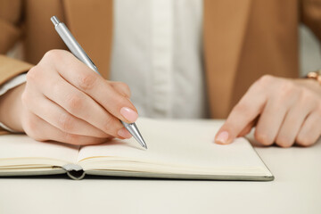 Woman writing in notebook at white table, closeup