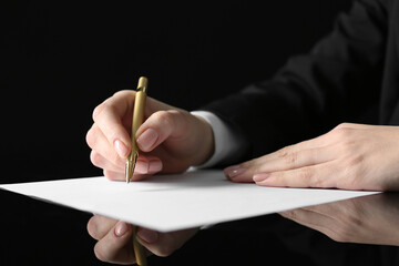 Woman writing on sheet of paper at glass table, closeup