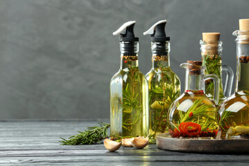 Cooking oil with different spices and herbs in bottles on grey wooden table. Space for text