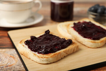 Delicious toasts with blueberry jam on wooden table, closeup