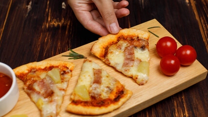 Closeup top view studio shot of three pieces of hot oven baked tasty delicious Italian homemade ham and pineapple Hawaiian soft bread crust pizza decorated on wooden plate pan with tomatoes ketchup