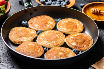 Pancakes in a frying pan with fresh berries and honey. 