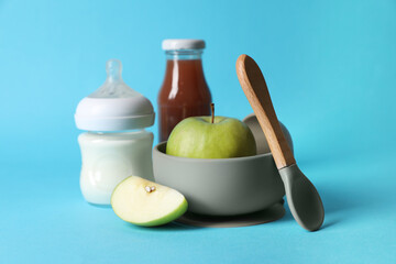 Healthy baby food, milk, apples and spoon on light blue background