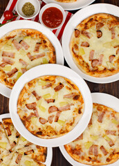 Closeup top view studio shot of multiple hot oven baked tasty delicious Italian homemade ham pineapple traditional Hawaiian bread crust pizzas placed on white dishes ready to serve in restaurant
