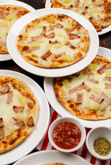 Closeup top view studio shot of multiple hot oven baked tasty delicious Italian homemade ham pineapple traditional Hawaiian bread crust pizzas placed on white dishes ready to serve in restaurant