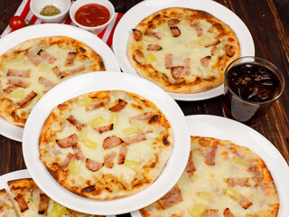 Closeup top view studio shot of multiple hot oven baked tasty delicious Italian homemade ham pineapple traditional Hawaiian bread crust pizzas placed on white dishes ready to serve in restaurant