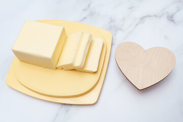 Freshly cut butter on a yellow plate and an empty wooden heart.