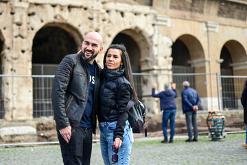 Fototapeta na wymiar Happy Beautiful Tourists couple traveling at Rome, Italy, poses in front of Colosseum at, Rome, Italy