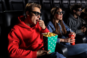 A man eats popcorn and watches a 3D movie at the cinema