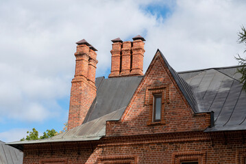 Red roof tiles with a red brick chimney on a blue sky background.