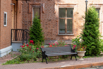 Wooden bench on the background of a brick house with flowers and trees.