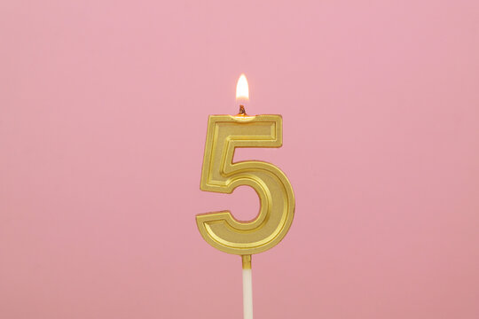 Burning gold birthday candle on pink background, number 5