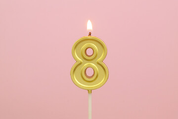 Gold birthday candle with shape number 8 burning on pink background.