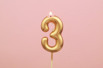 Burning gold birthday candle on pink, shape number 3