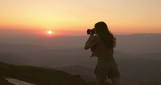 Cinematic shot of mountain valley at red-orange sunset and woman amateur photographer with dslr camera taking pictures of scenic landscapes. Woman amateur photographer takes photos. Tourism and travel
