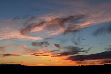 Large ranch house silhouette in the distance at the horizon dwarfed by sunrise or sunset in Montana for scale to show big sky country