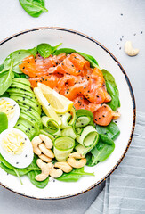 Keto salad bowl with salmon, avocado, spinach, cucumber, eggs, cashew nuts. Low-carbohydrate breakfast rich in healthy fats. White table background, top view