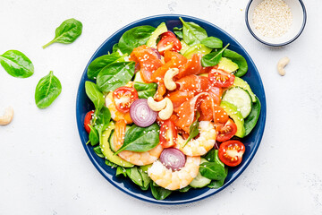 Ketogenic diet salad with salmon, shrimp, avocado, spinach, cucumber, tomato, cashew nuts, sesame. Low-carbohydrate lunch rich in healthy fats. White table background, top view