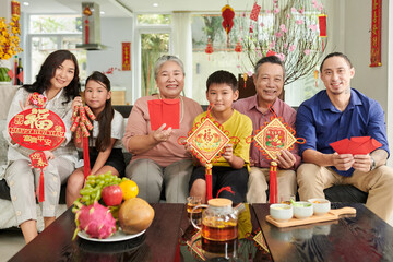 Joyful three generation family showing Chinese New Year decorations and smiling at camera