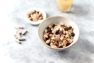 Bowl of granola with nuts,  cranberry, almonds and rasins. Sport supplements ( carnitine capsules ) in background. Bright stone  background. 