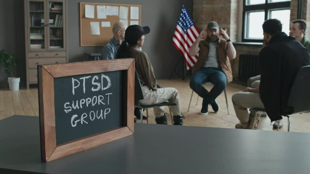 Selective focus shot of small blackboard with chalk inscription in wooden frame on table, PTSD support group discussing problems on background