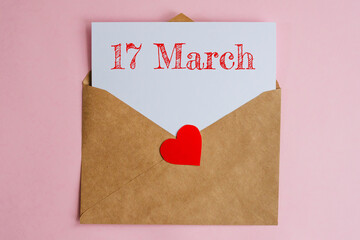 Kraft envelope with a white sheet of paper and a date 17 march, with a red heart. Flat lay on pink background, romance and love concept