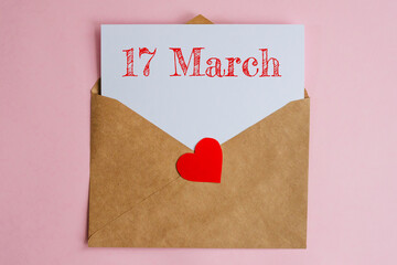 Kraft envelope with a white sheet of paper and a date 17 march, with a red heart. Flat lay on pink...
