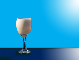 White milk in a clear glass. Blue background and white sun rays on the sides (bottom and top).