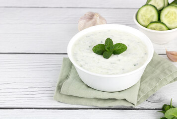 Indian raita sauce with dahi yogurt, cucumber and herbs on a white wooden background. copy space. Greek tzatziki sauce. 