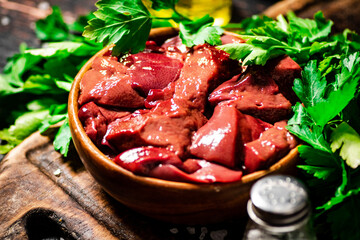 Pieces of raw liver in a bowl on a parsley cutting board.