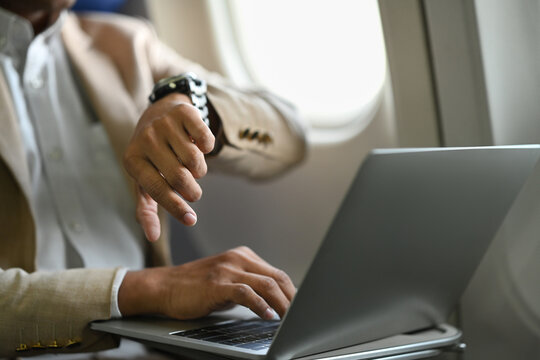 Cropped image of businessman in suit checking arrival time on his watch while sitting in airplane cabin
