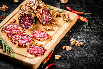 Pieces of salami sausage on a cutting board with pods of dried chili peppers. 