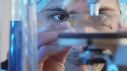 Closeup on focused eyes. The laboratory assistant puts the object of study on the microscope. A man of Asian appearance works in a laboratory.