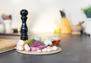 Raw wrap beef steak and variety ingredient on circle wicker plate with sauce, salt and butter in mini glass bowl on black granite kitchen counter surface.