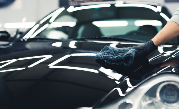Close-up shot of man wearing black glove applying ceramic coating to hood of black car. Professional car detailing. Horizontal indoor shot. High quality photo