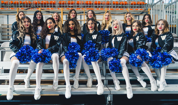Female cheerleaders sitting in two rows. They are wearing black baseball hoodies. High quality photo