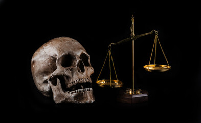 Golden scales and a human skull on a black background