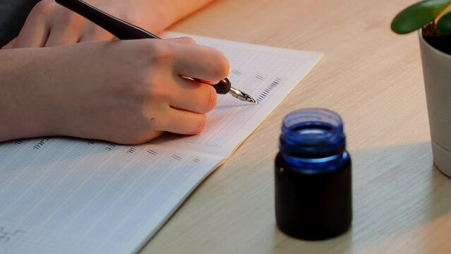 A girl sits at the table and writes with a pen and ink. Calligraphy, handwriting correction, beautiful writing.