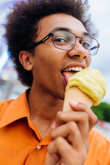 Handsome young black man eating ice cream at amusement park - Cheerful african-american male portrait during summertime vacation- Leisure, people and lifestyle concepts