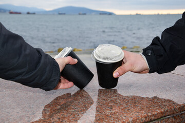 Two paper coffee cups stand on a marble border. Male hands take glasses of coffee against the...