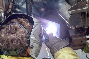 Worker welding the iron parts of a machine.