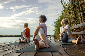 Fototapeta premium Group of senior woman doing yoga exercises by the lake.